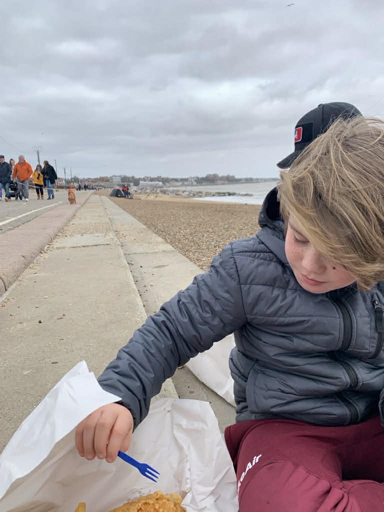 boy eating fish and chips on felixstowe beach in the winter