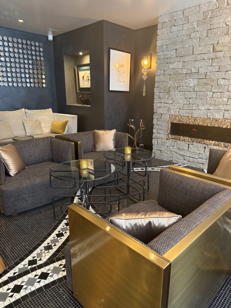 The stylish lounge bar at The One Alma Paris with gold-framed armchairs, stone fireplace and mosaic tiled floor